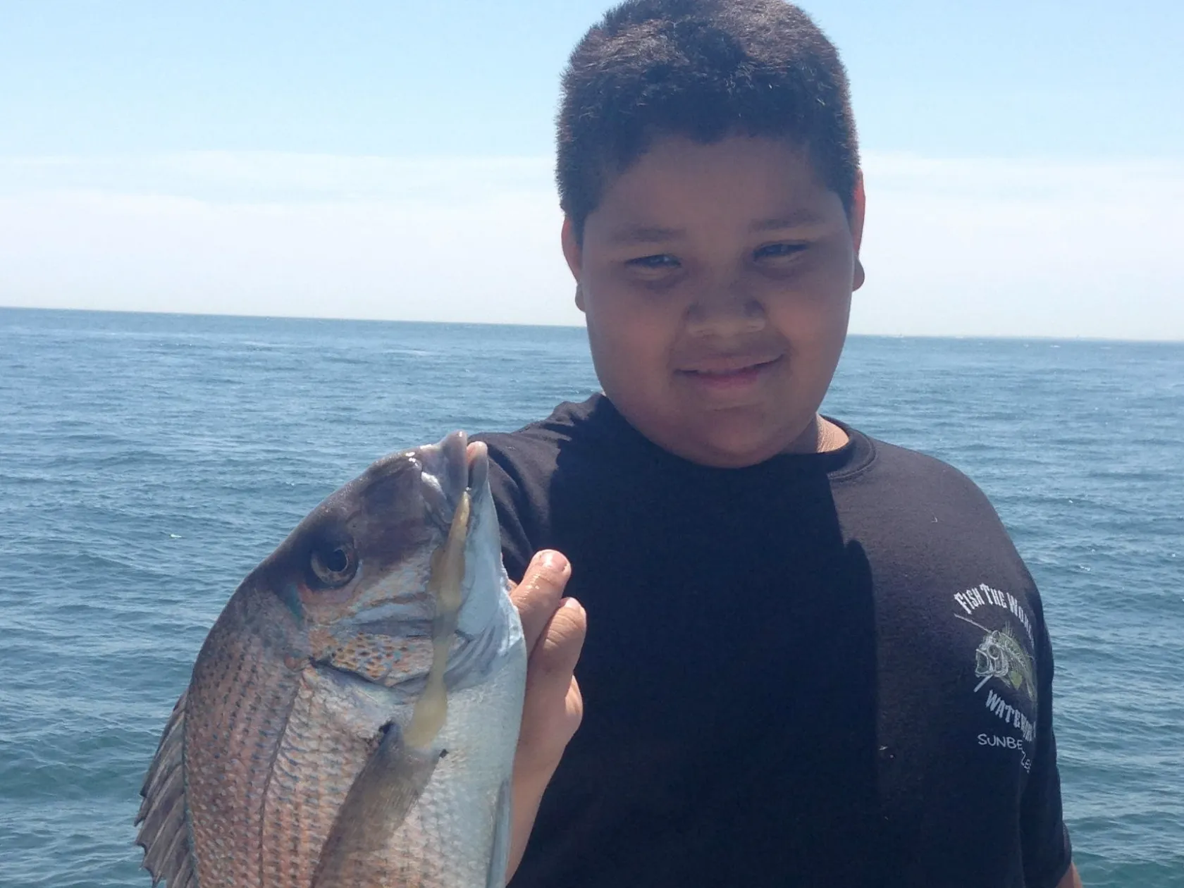 a man holding a fish in front of a body of water