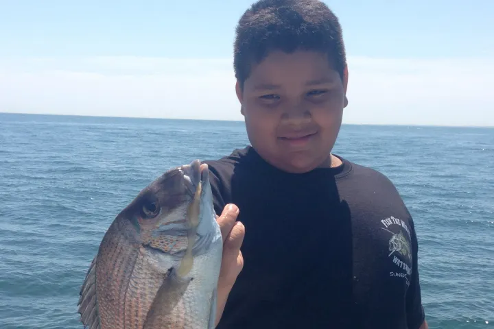 a man holding a fish in front of a body of water